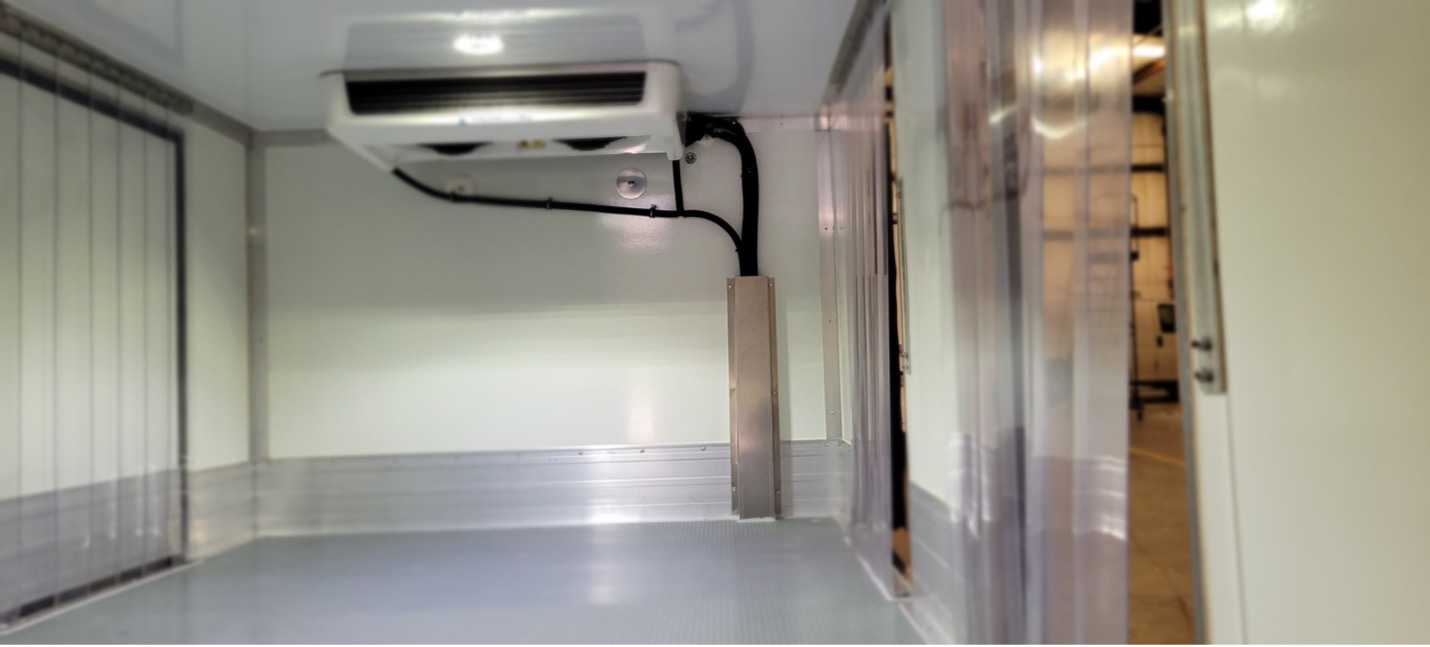 Interior of refrigerated cargo van with wall insulation, strip curtains, and ceiling-mounted cooling unit.