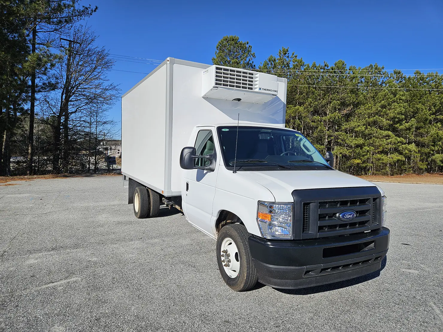 White refrigerated box truck with a nose-mounted Thermo King refrigeration unit parked on pavement.